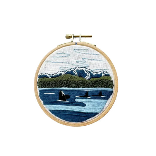 Embroidery hoop with a scenic landscape of mountains, trees, and water.