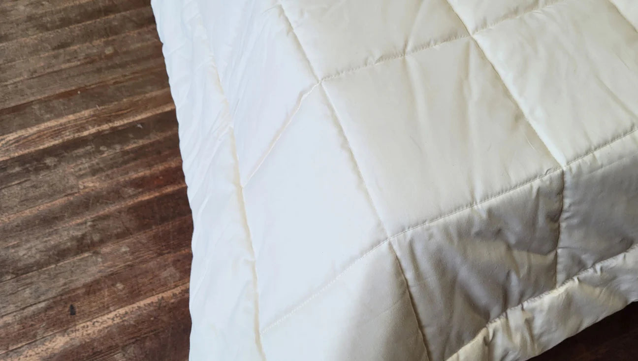 Edge of quilted cotton comforter draped over bed showing thickness and natural texture