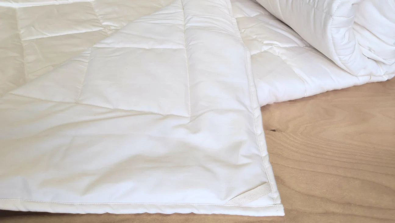 Organic cotton comforter laid flat on bed showing smooth quilted surface and natural color