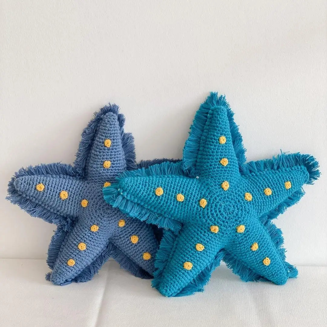 Two handmade organic cotton crochet starfish soft toys in blue and lagoon blue, featuring yellow stitched spots and fringed edges.