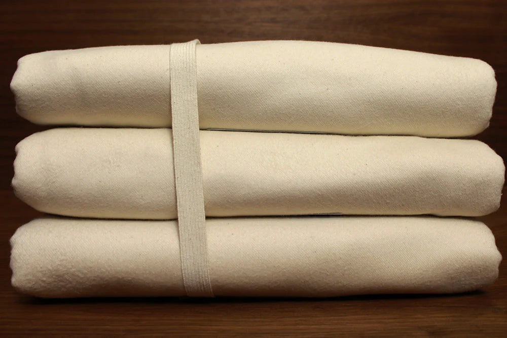 Folded organic cotton mattress protectors in a natural cream color with visible woven texture