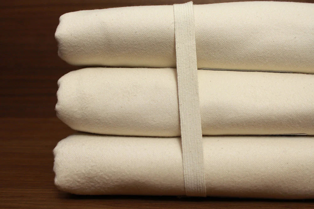 Stack of folded organic cotton mattress protectors in a natural cream off-white color