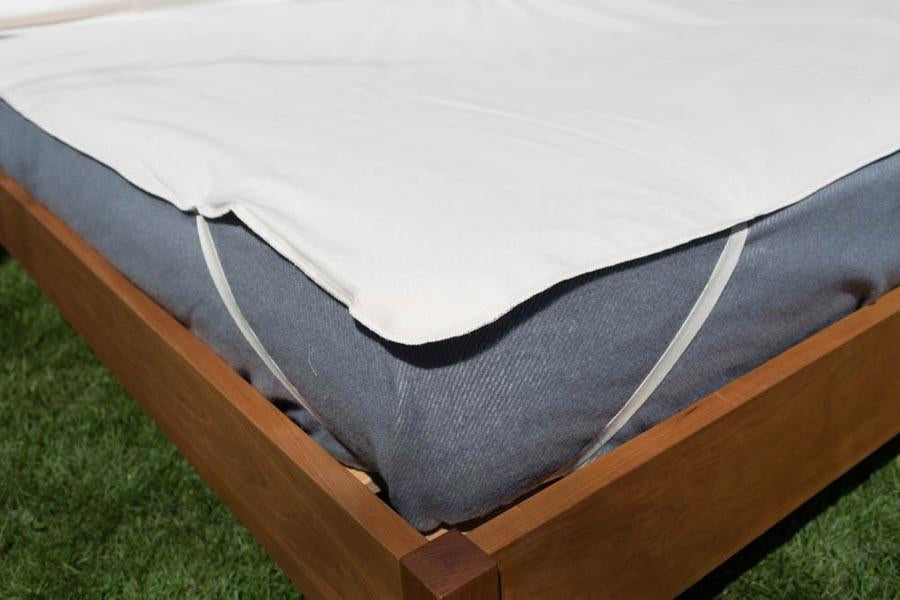 Organic cotton mattress protector secured over a mattress with corner straps