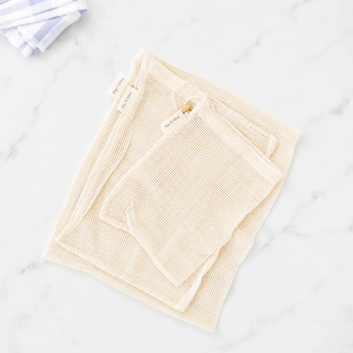 Set of three organic cotton mesh produce bags in small, medium, and large sizes with drawstring closures and tare weight tags