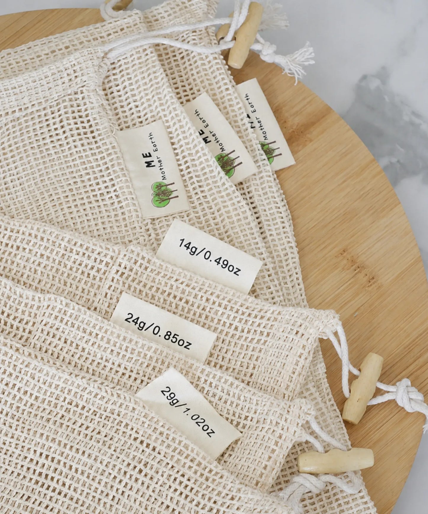 Organic cotton mesh produce bags with drawstring closures displaying front brand tags and tare weight tags for small, medium, and large sizes.