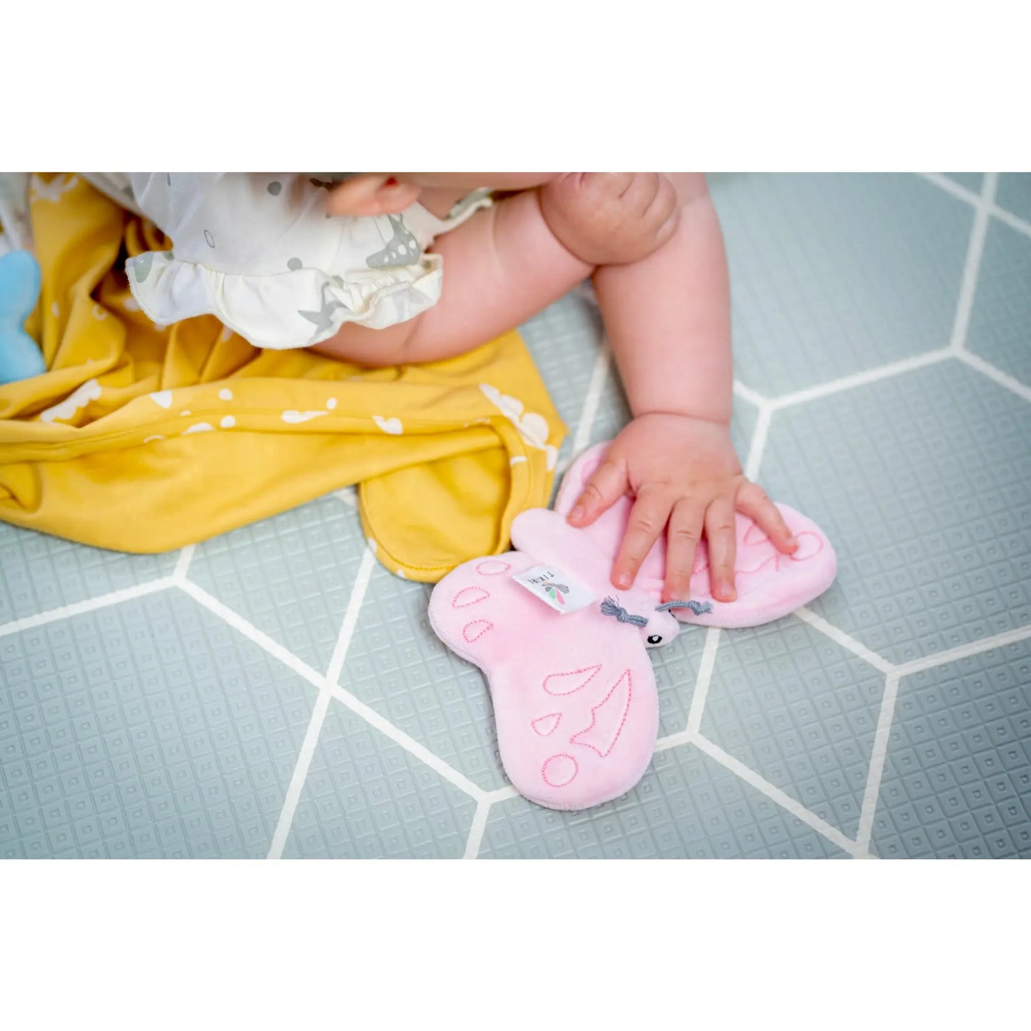 Infant playing on the floor with a pink butterfly crinkle toy