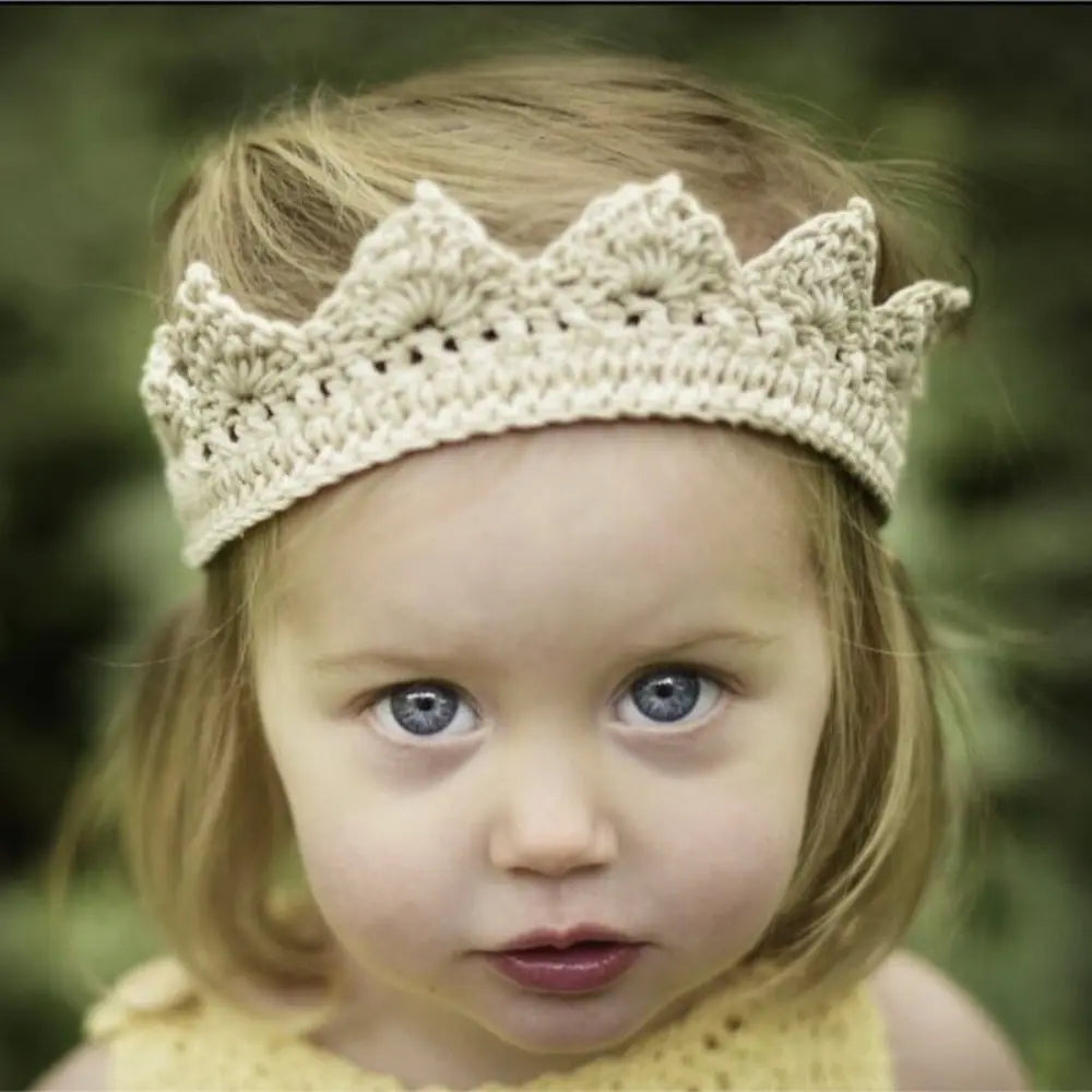 Young child wearing a beige crochet crown with a blurred green background