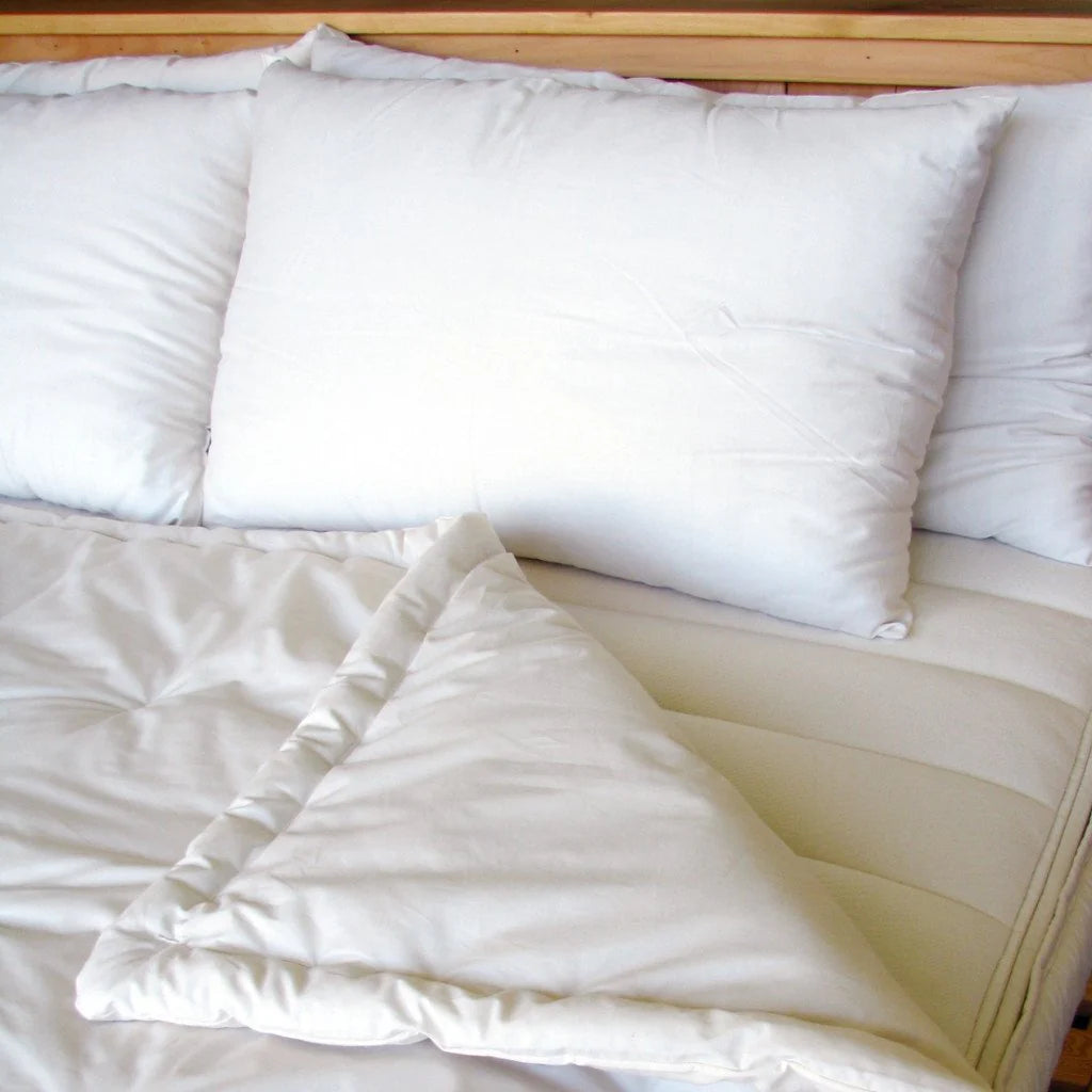 Folded wool comforter on bed with pillows showing soft drape and natural texture