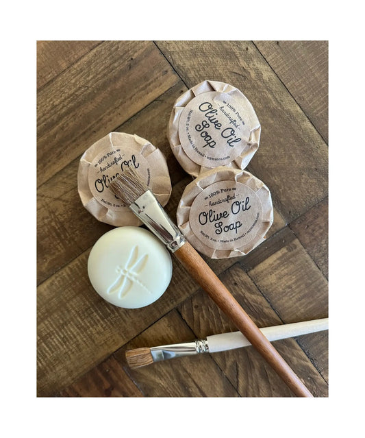 two paintbrushes with olive oil soap bars on a wooden table top