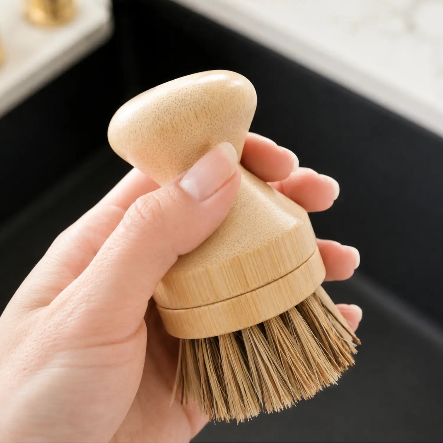 Close-up of a modular bamboo dish brush with dark palm and sisal bristles held in one hand.