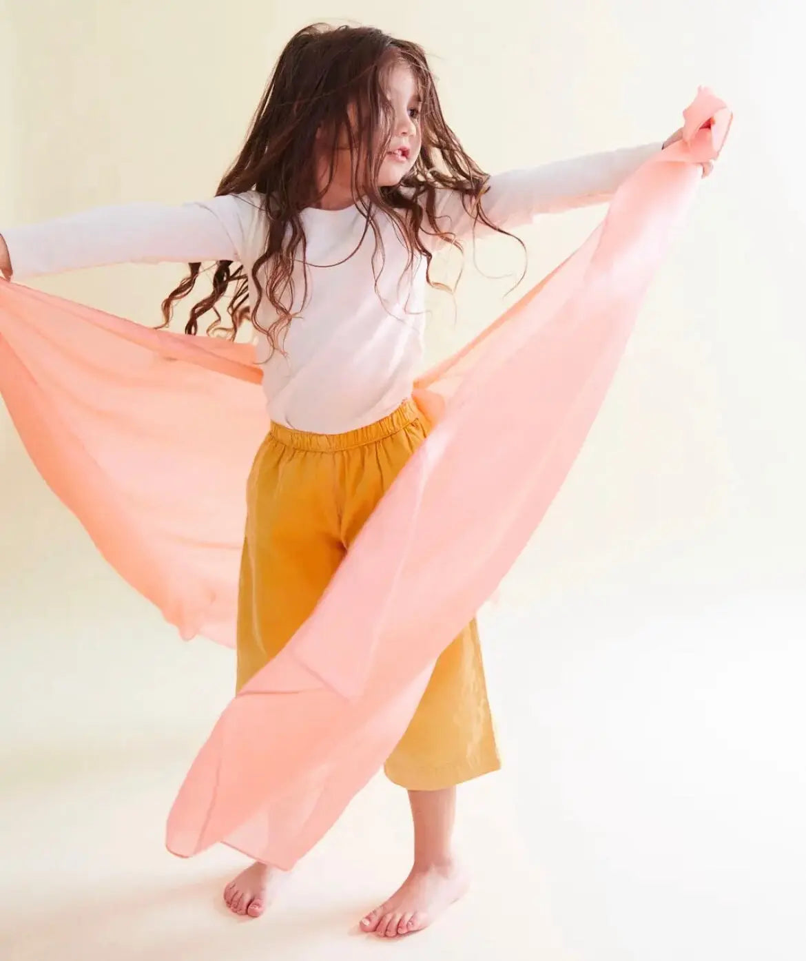 Girl holding a peach playsilk in outstretched arms with the silk billowing