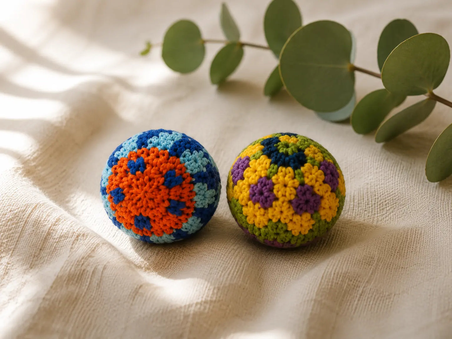 Two handmade crocheted cotton balls with colorful floral patterns on a beige linen fabric