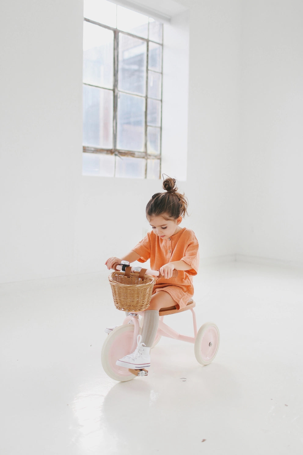 Child riding a tricycle with a basket in a bright room
