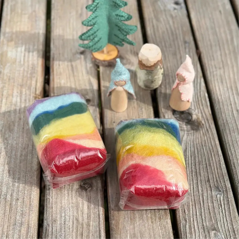 Two bags of rainbow colored wool with peg dolls and felt tree on a wooden table