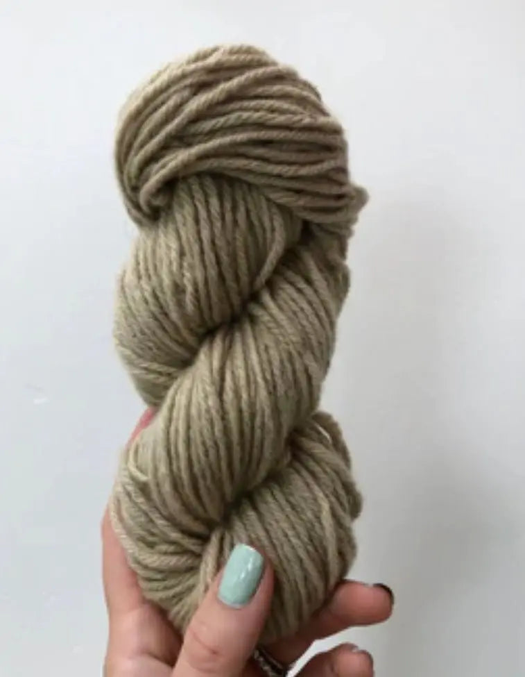 Hand holding a skein of beige yarn against a white background
