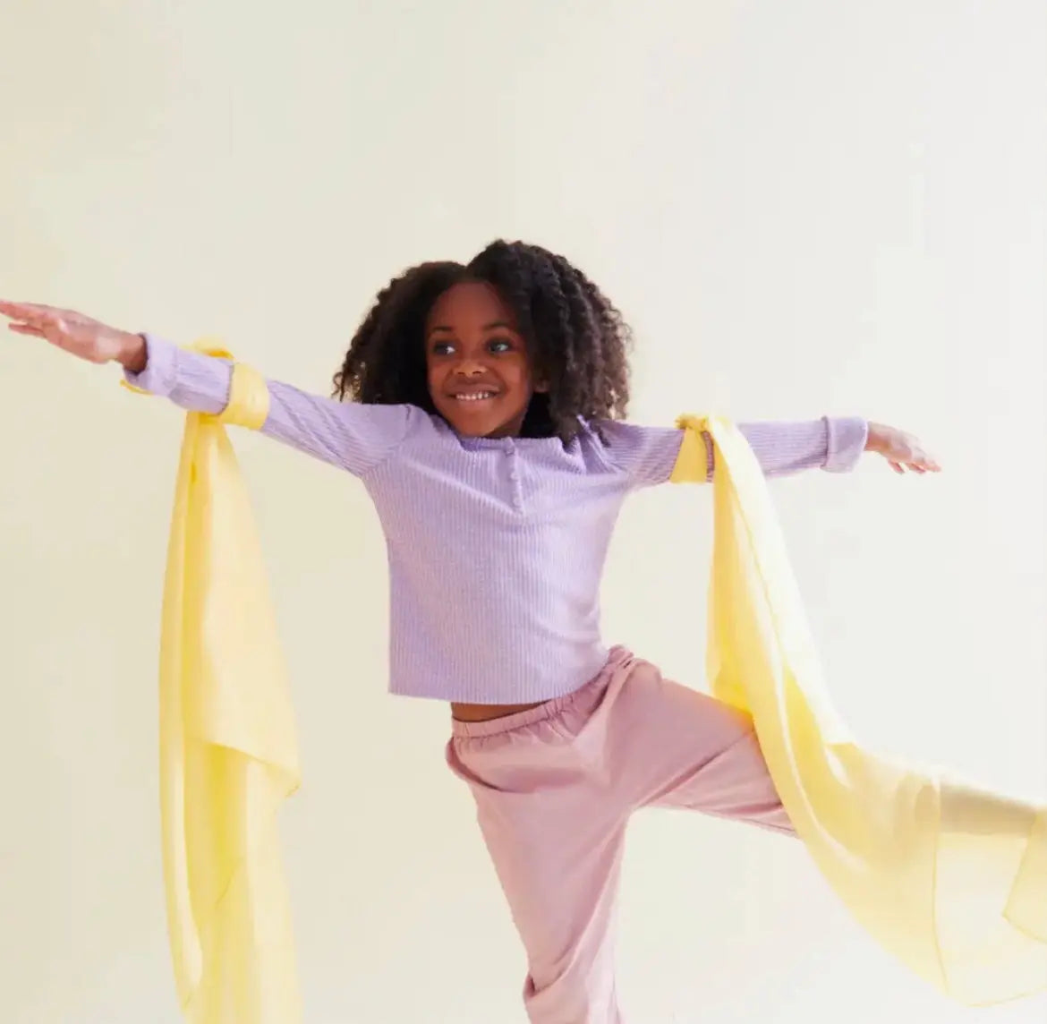 Girl with two sunshine yellow playsilks tied to her arms playing