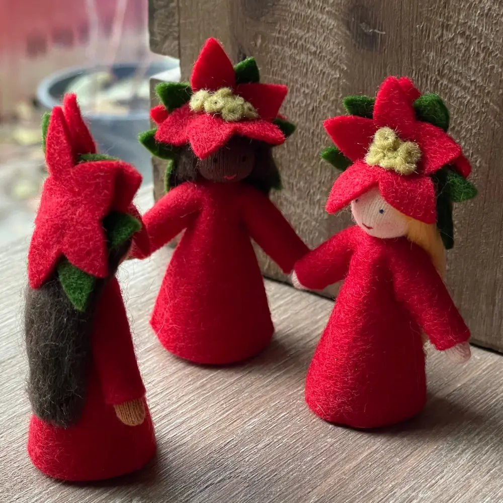 Three red flower-shaped dolls with green stems on a wooden surface.