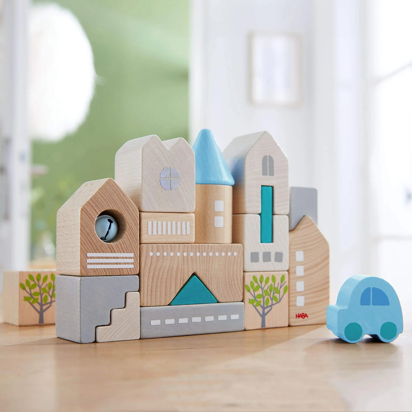 Wooden toy blocks shaped like buildings and a car on a light surface with a blurred background