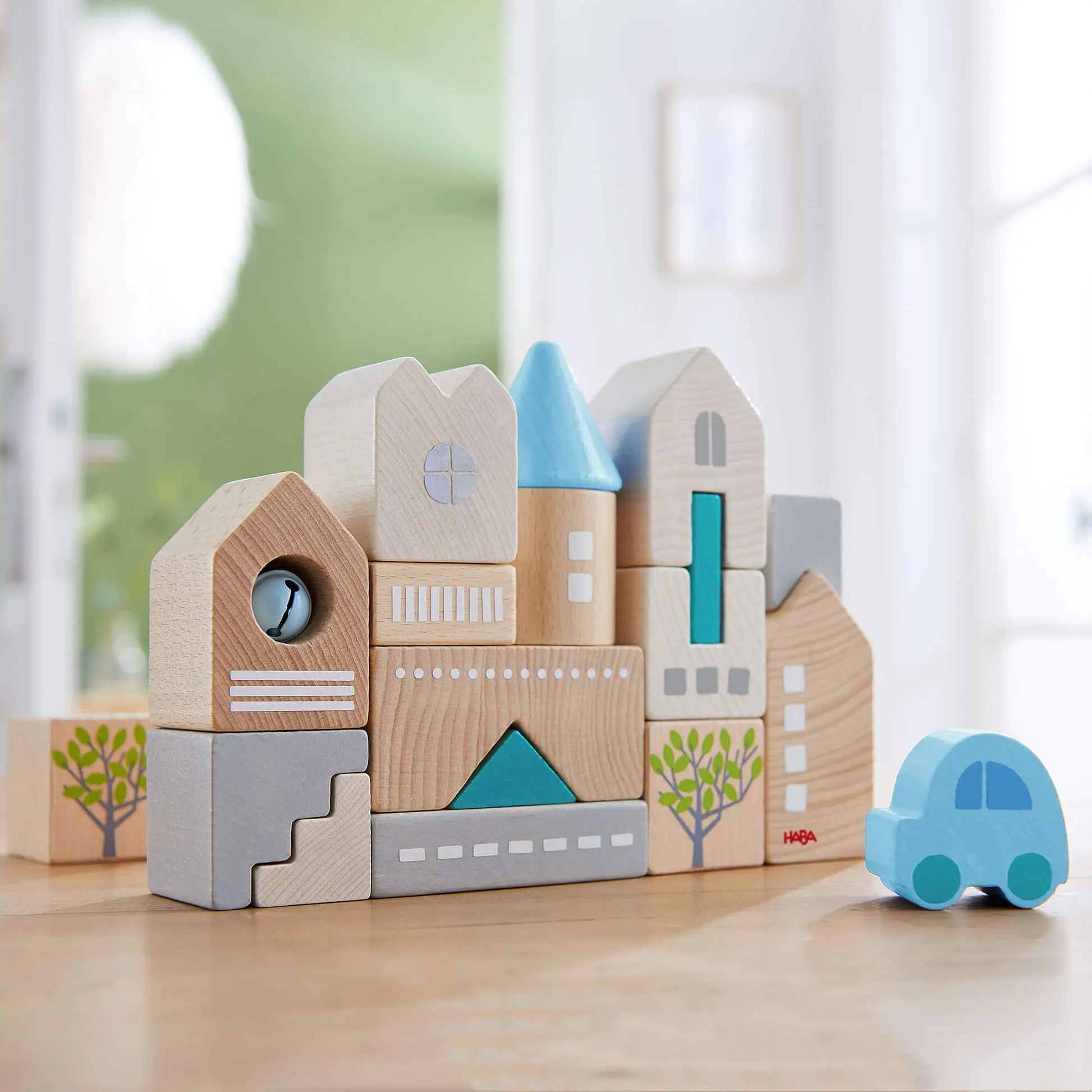 Wooden toy blocks shaped like buildings and a car on a light surface with a blurred background