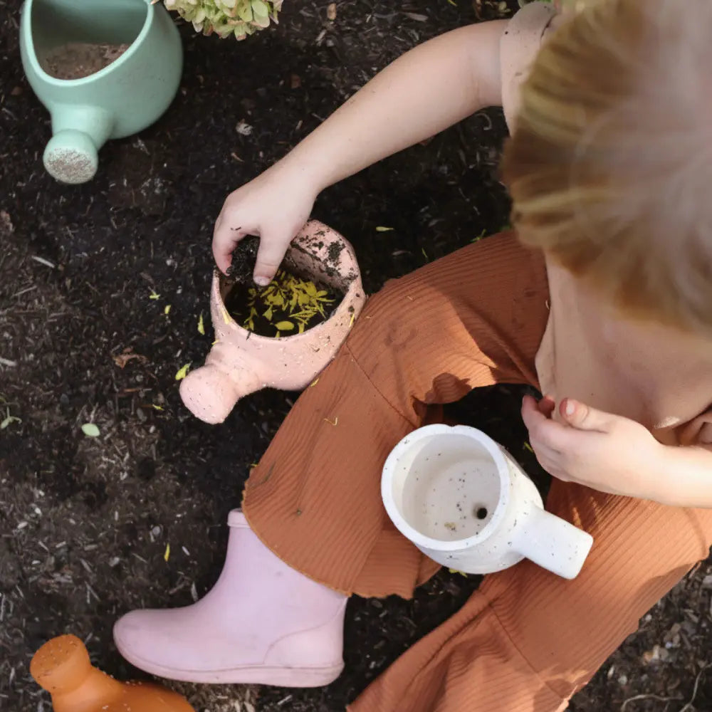 Preschooler sitting on the ground with silicone gardening tools 