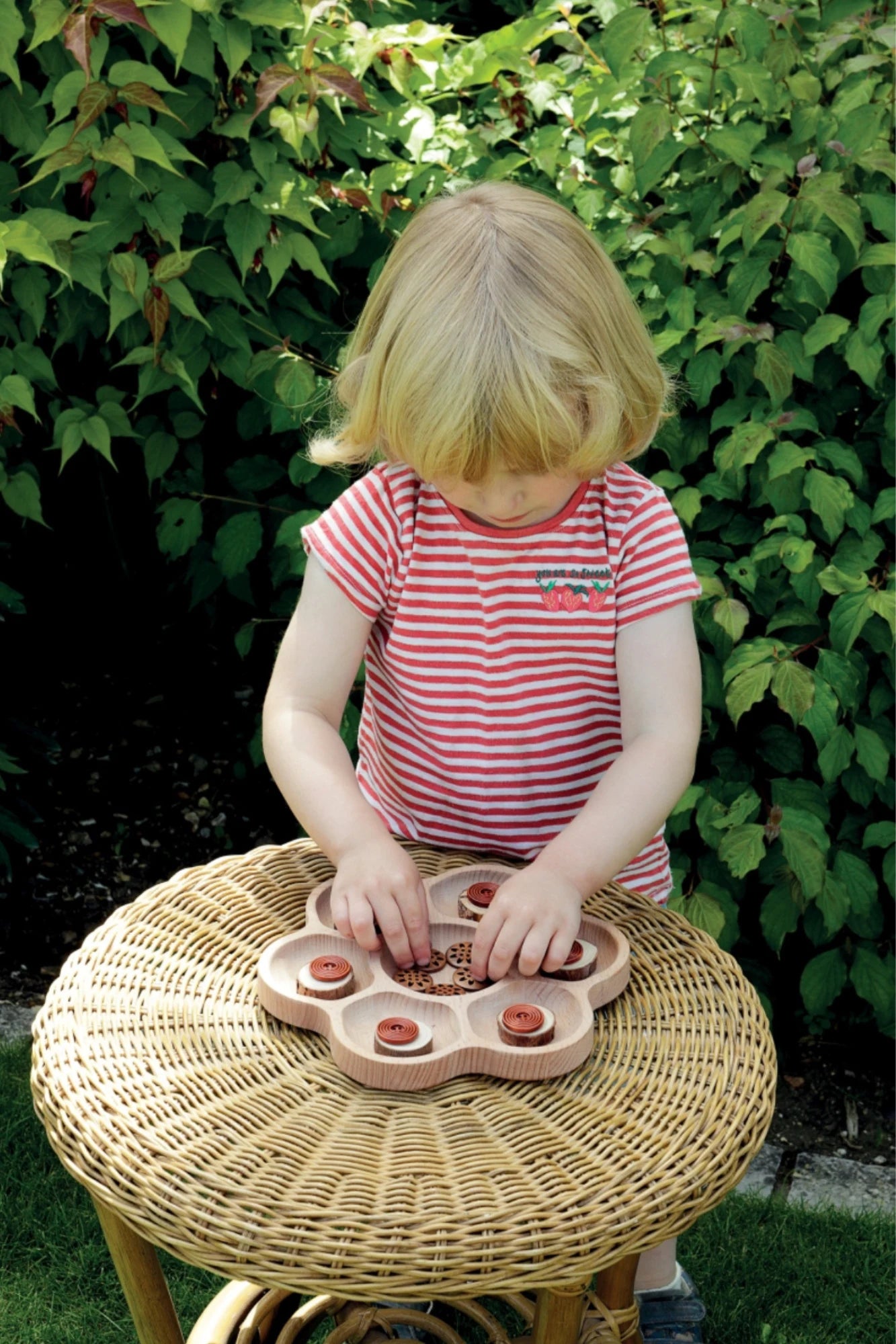 A child using a sorting tray outside sorting wood pieces and stones