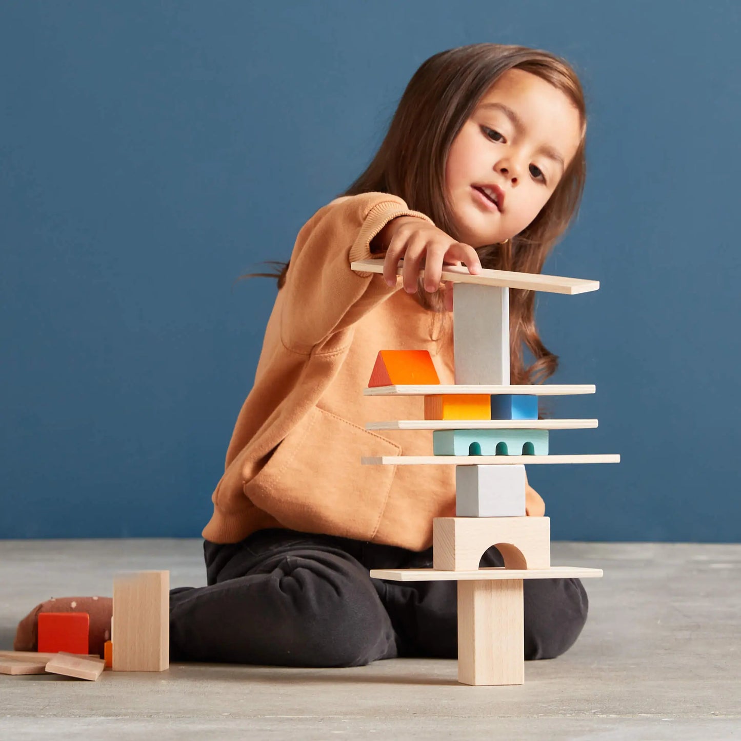 Child playing with wooden building blocks against a blue background