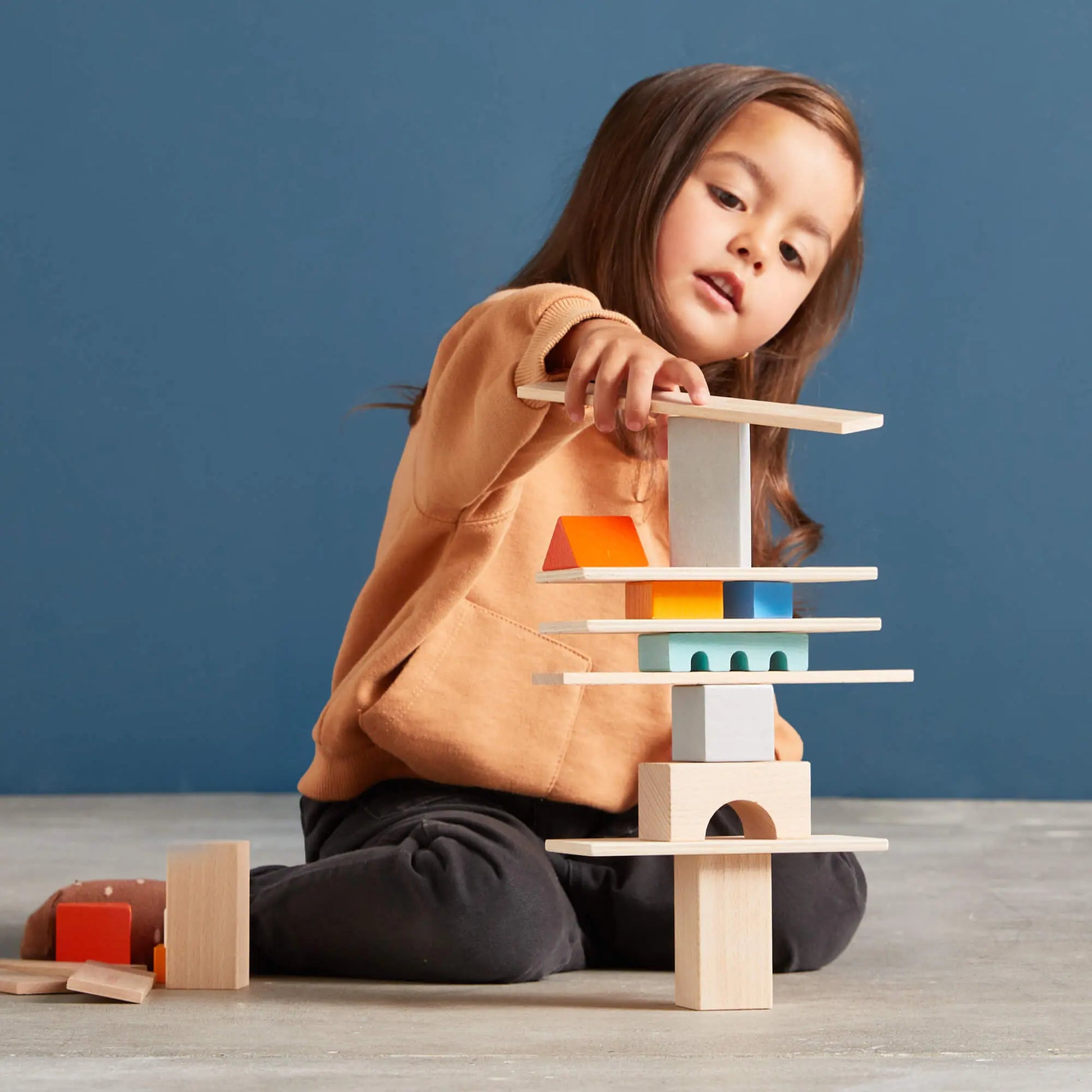 Child playing with wooden building blocks against a blue background