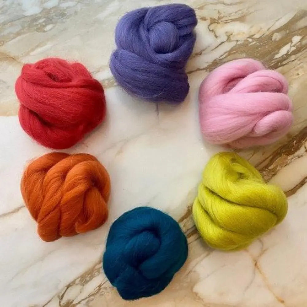 Six skeins of wool comb top in red, purple, pink, orange, blue, and yellow on marble background