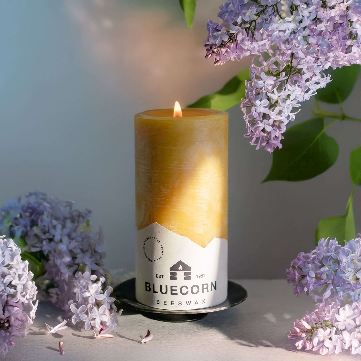 Candle with Bluecorn Beeswax label surrounded by lilac flowers