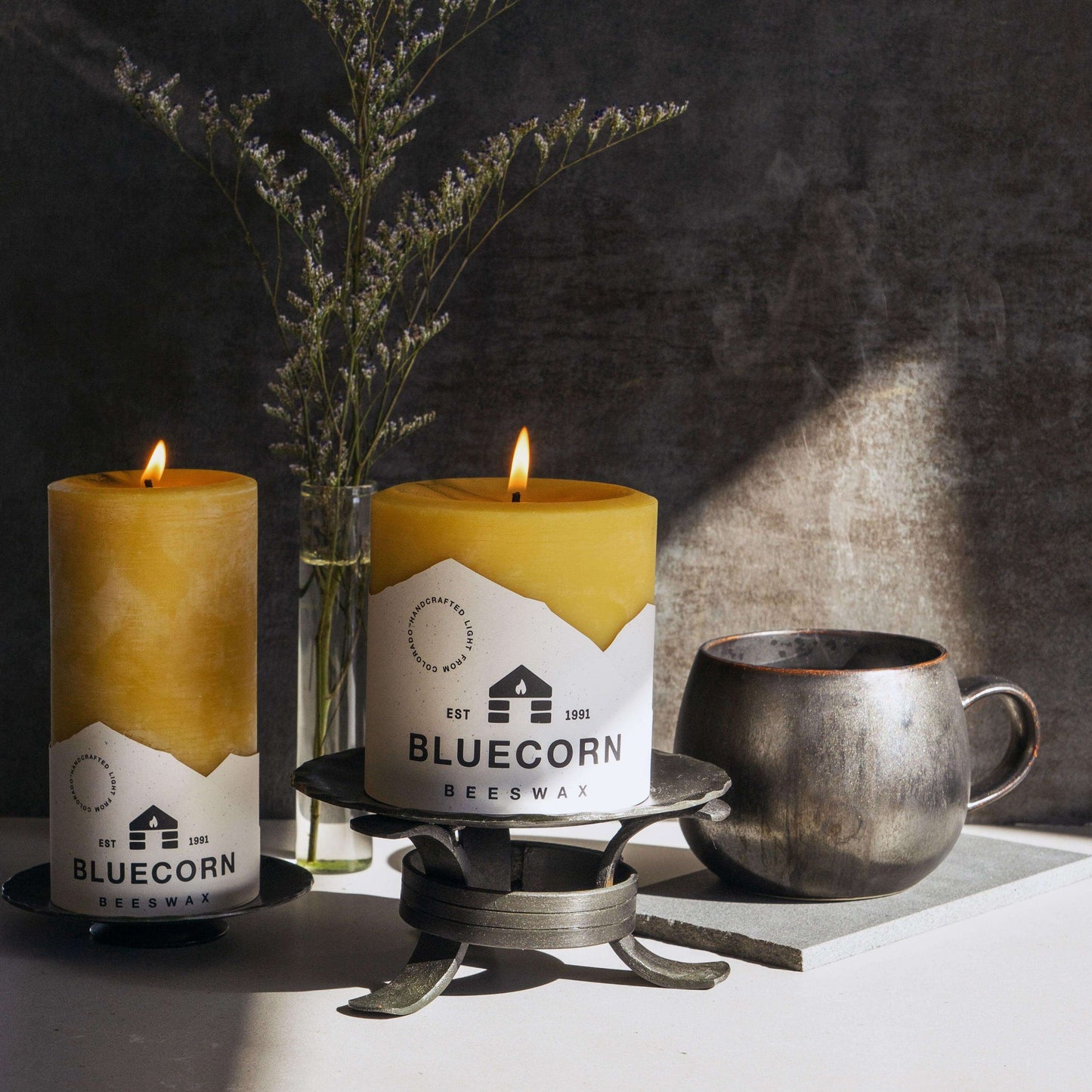 Two lit candles with 'Bluecorn' branding on a dark background