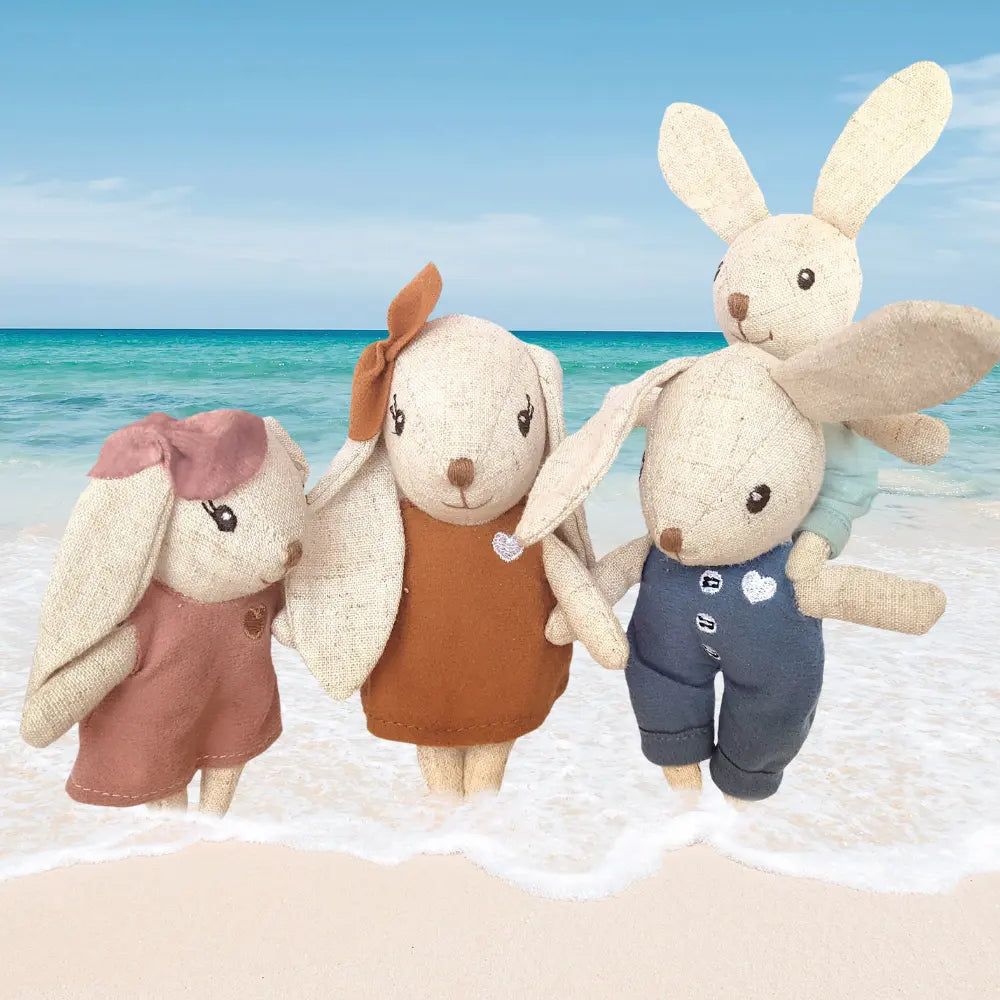Four plush linen rabbit toys  close-up in different outfits on a beach background