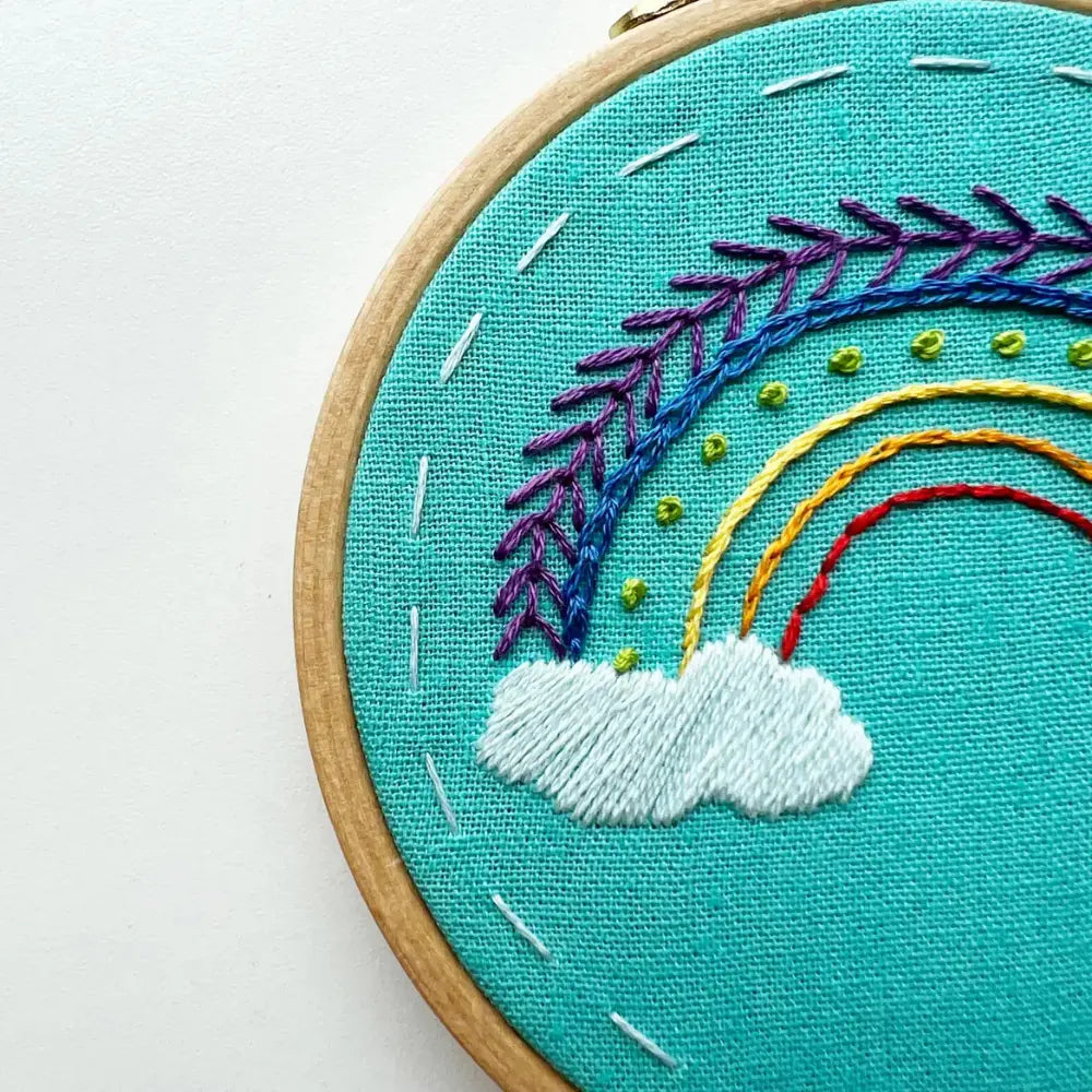 Detailed close-up of rainbow and cloud embroidery stitches on turquoise fabric in beginner embroidery kit