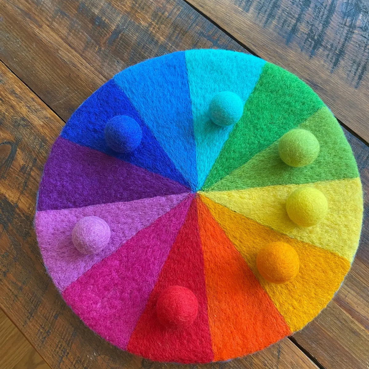 12-color rainbow felt play mat with matching wool balls photographed on a wooden table