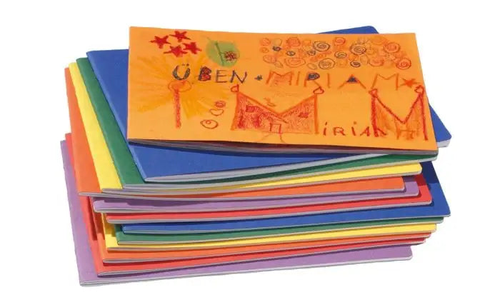 Stack of colorful main lesson books with one pad featuring child-like drawings on a white background