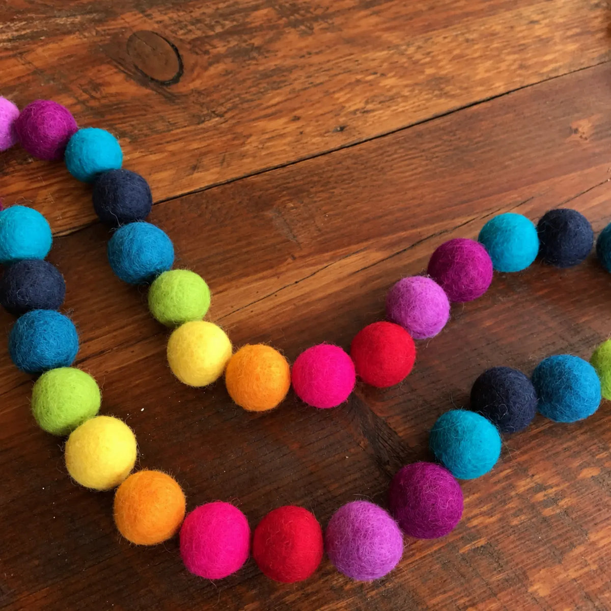 Rainbow wool felt balls arranged in a curved line on a wooden surface.
