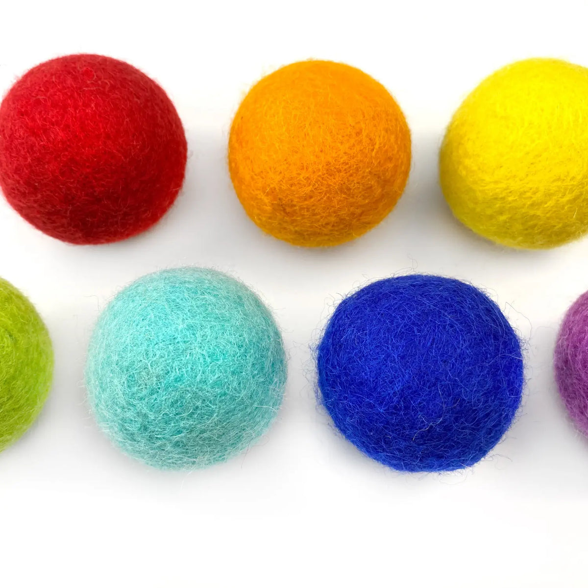 Close-up of red, orange, yellow, green, turquoise, and blue wool felt balls showing their fuzzy hand-felted texture.