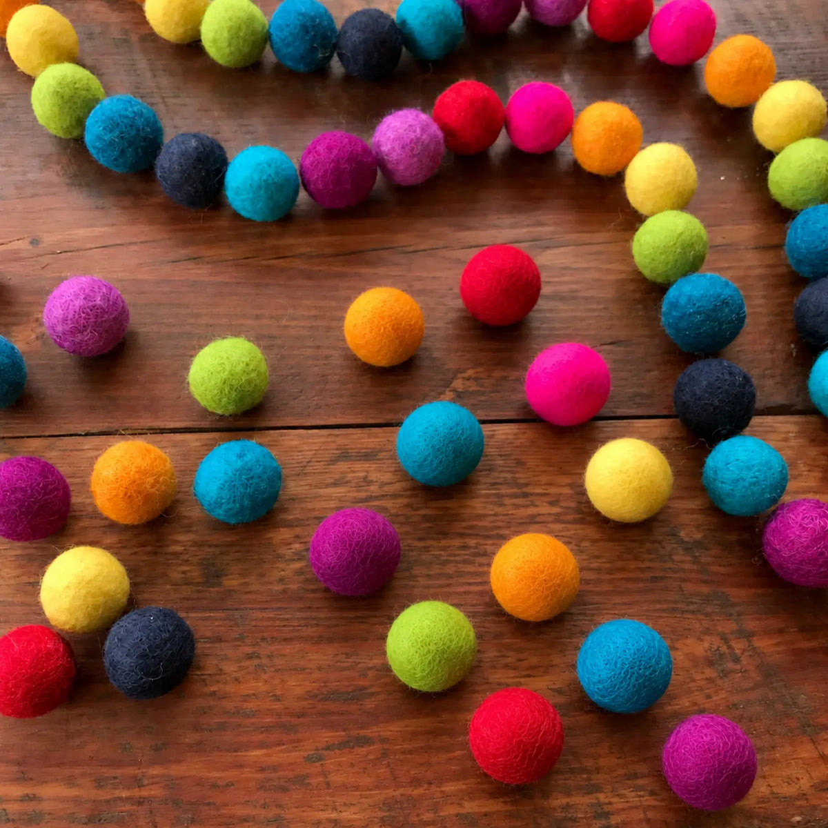 Rainbow wool felt balls scattered across a wooden surface.