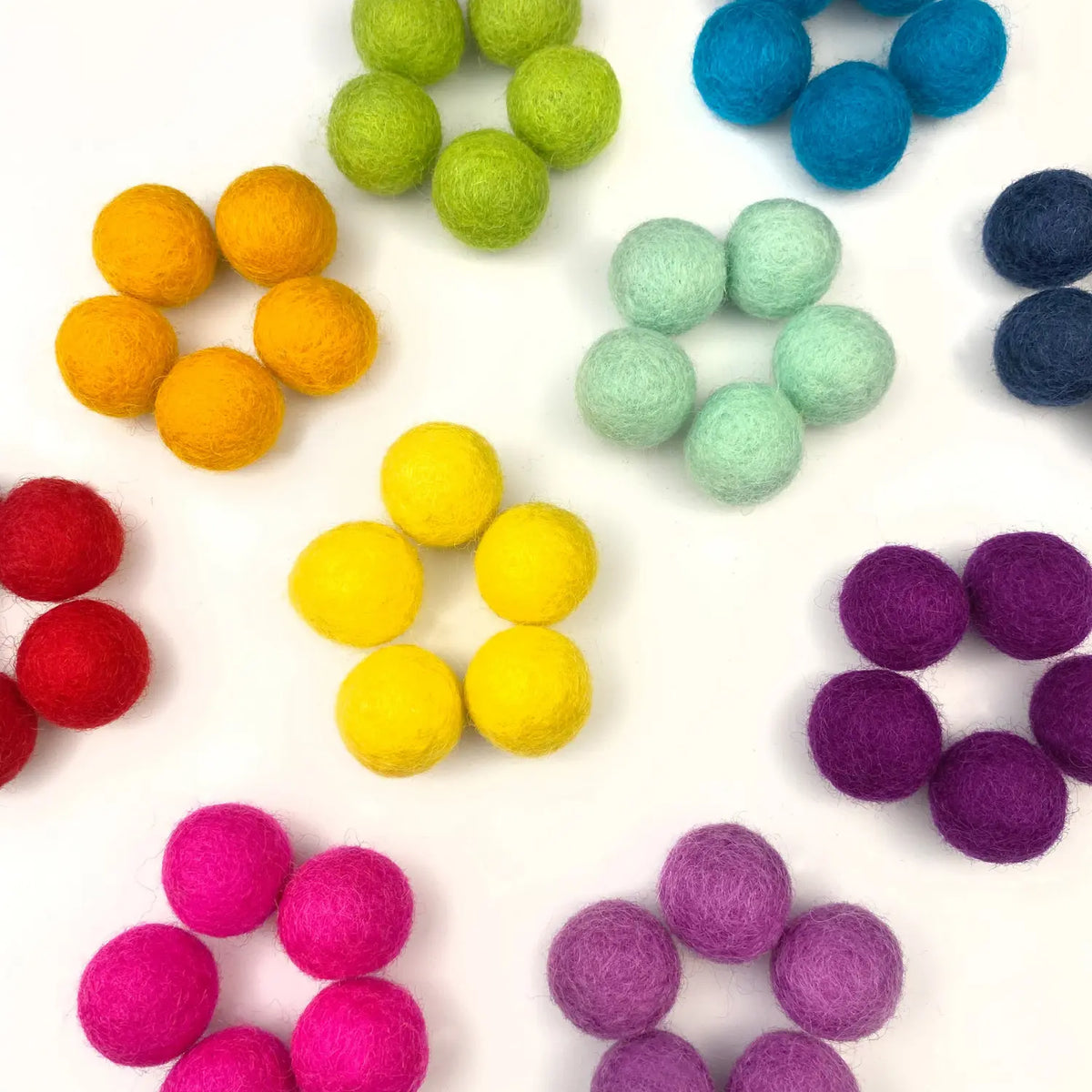 Handmade wool felt balls grouped by color groups of five on a white background.