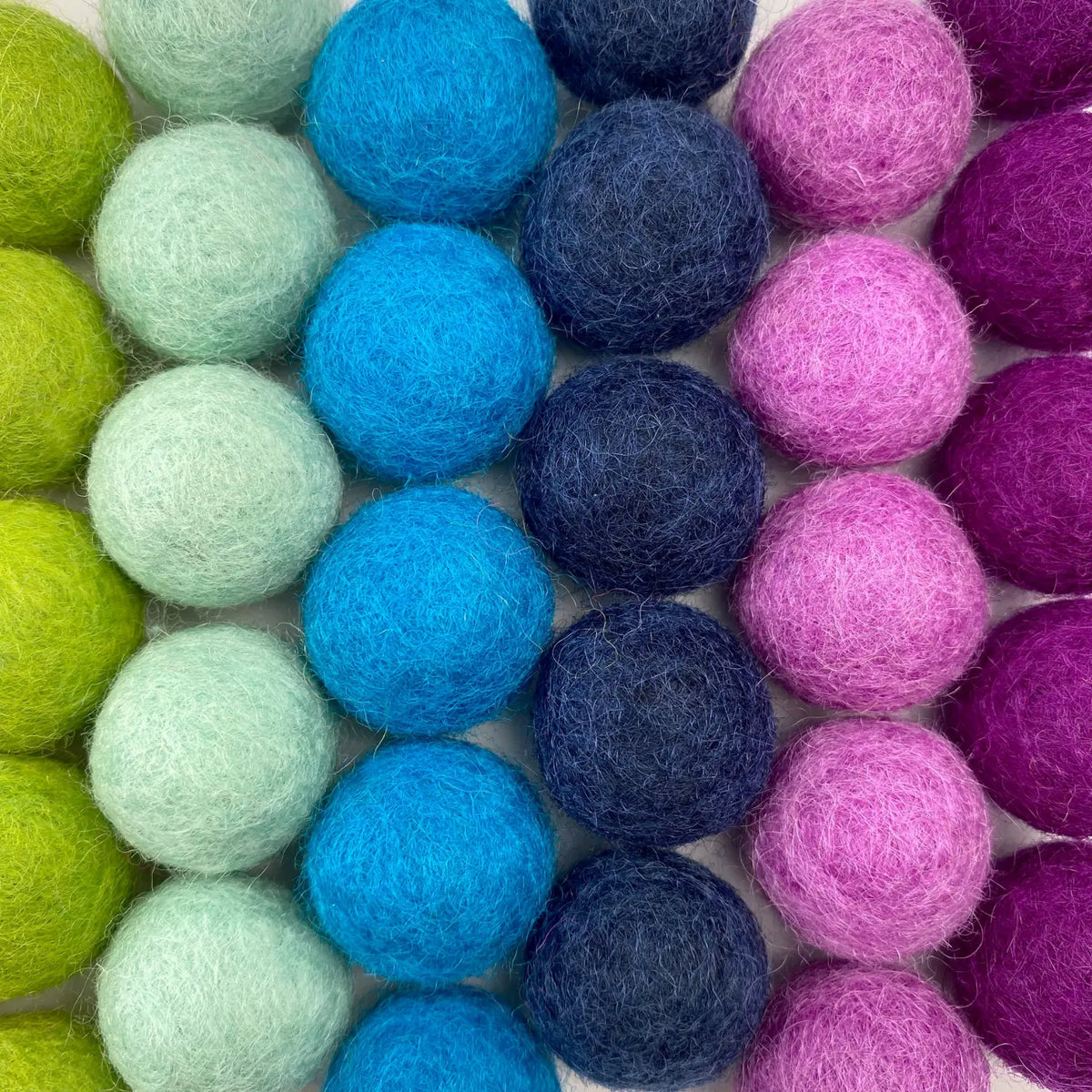 Close-up of blue, teal, indigo, and pink wool felt balls showing their soft felted texture.