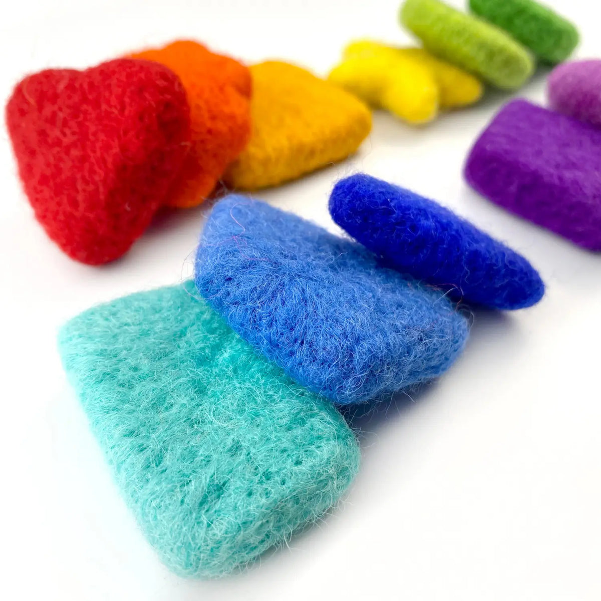 Close-up of turquoise and blue wool felt shapes stacked in front of red, orange, yellow, and green felt shapes.