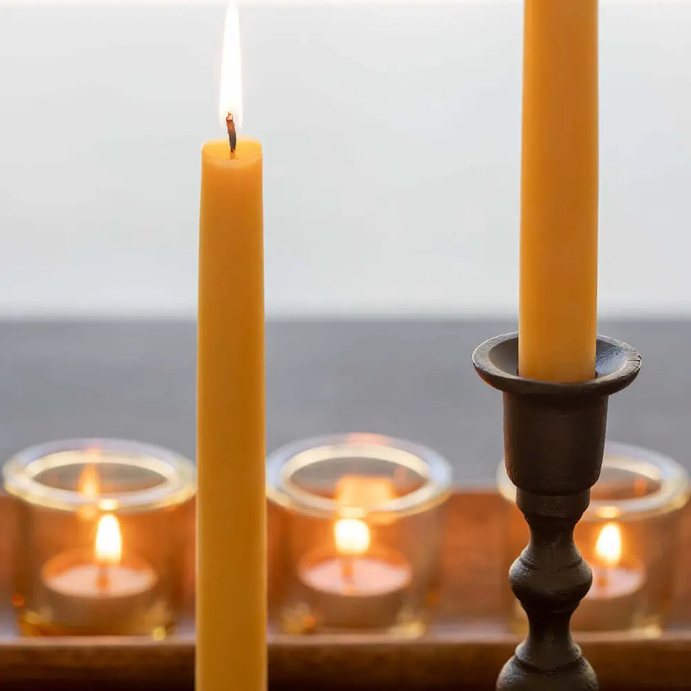 Two lit beeswax candles in wooden candle holders with a blurred background