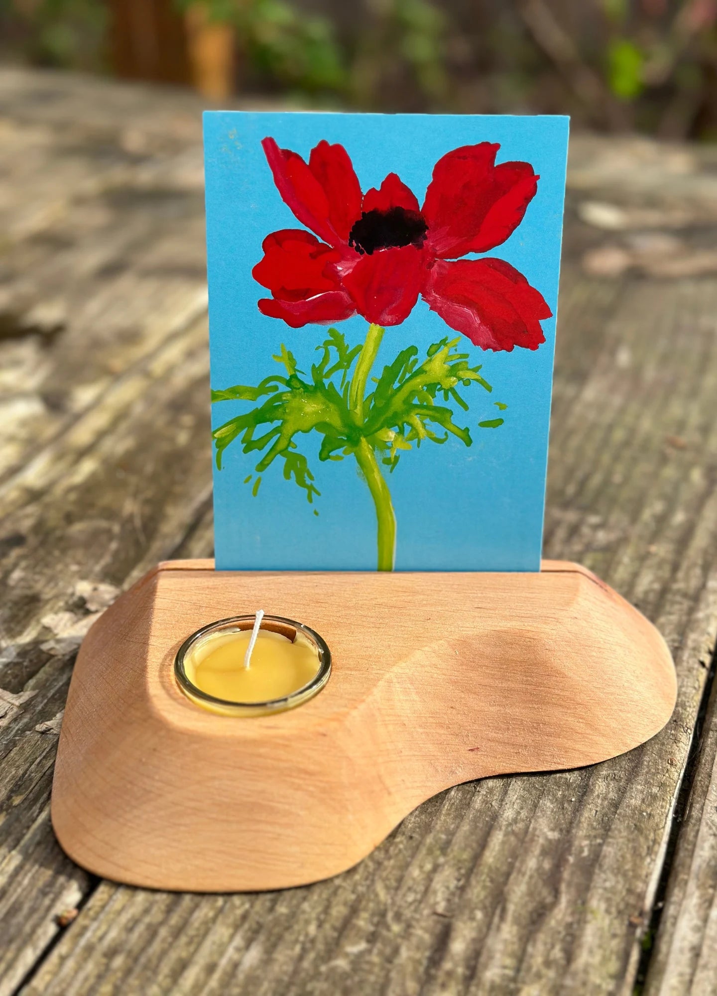 Red anemone flower in an alderwood postcard holder with beeswax candle