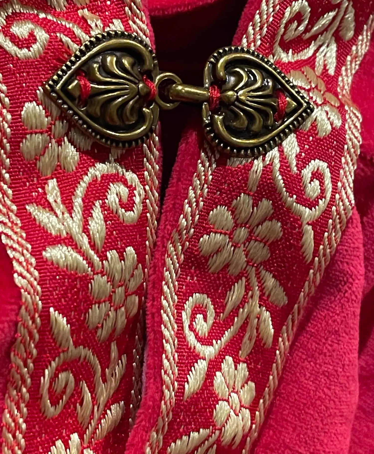 Close-up of gold jacquard ribbon trim and metal clasp on red velour dress-up cape