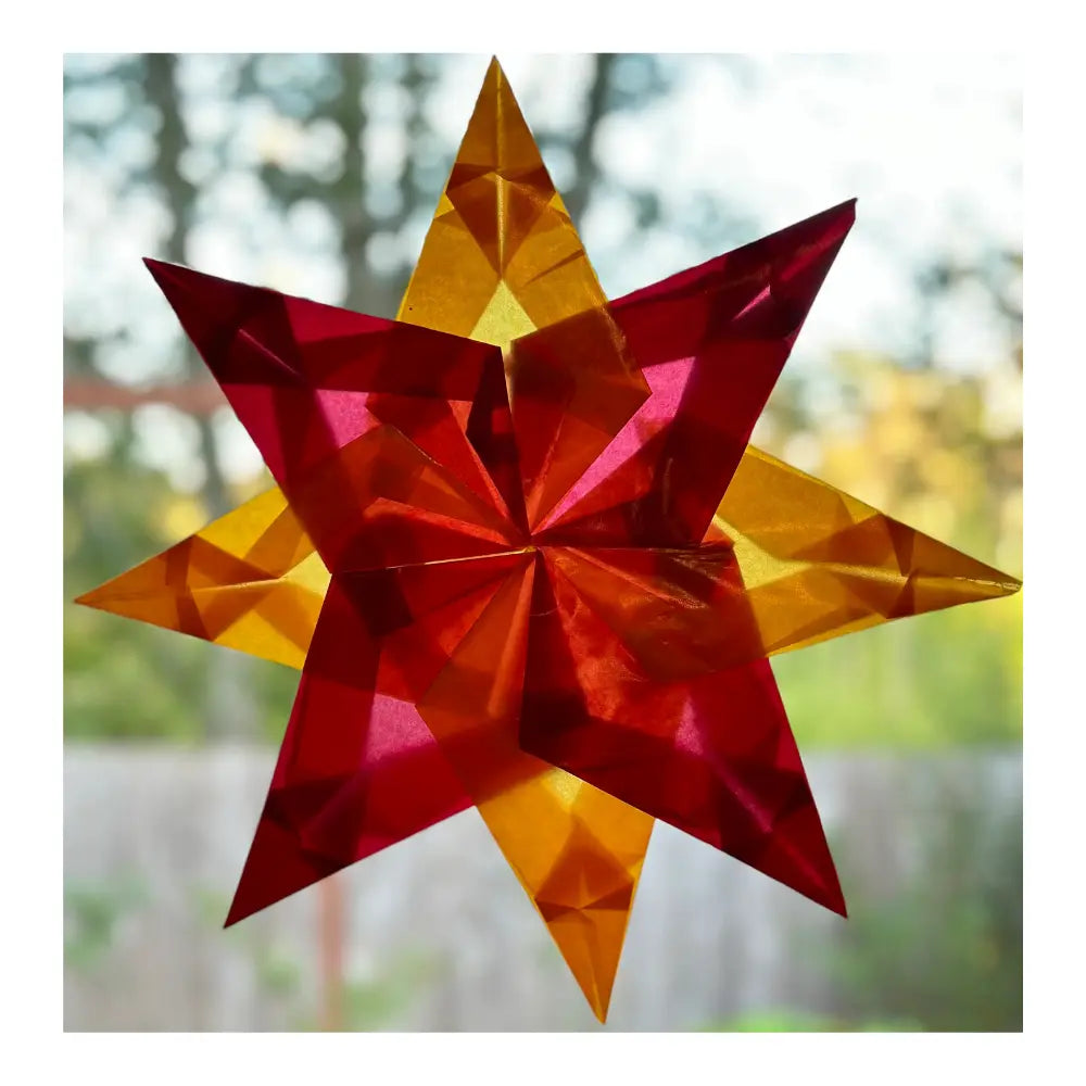 Red window star crafted from translucent kite paper with light shining through