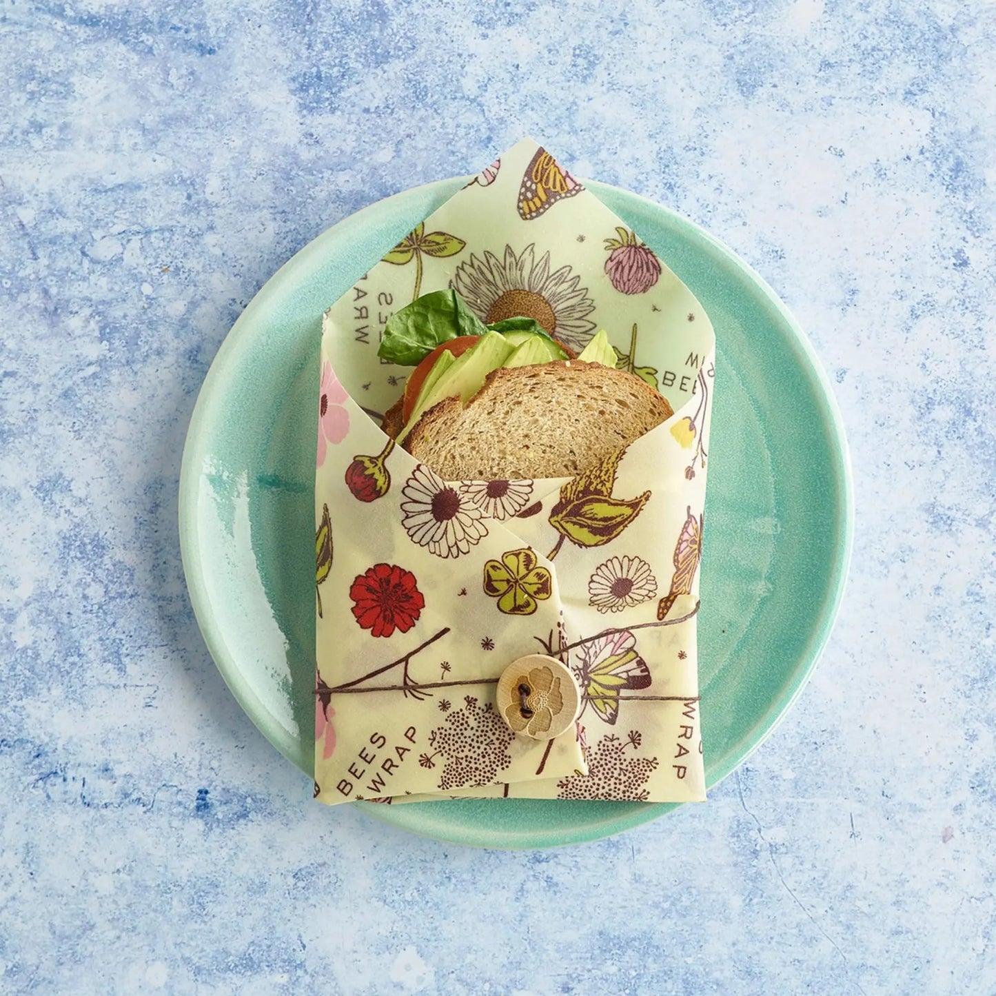 Sandwich wrapped in a vegan food wrap with floral design on a blue plate.
