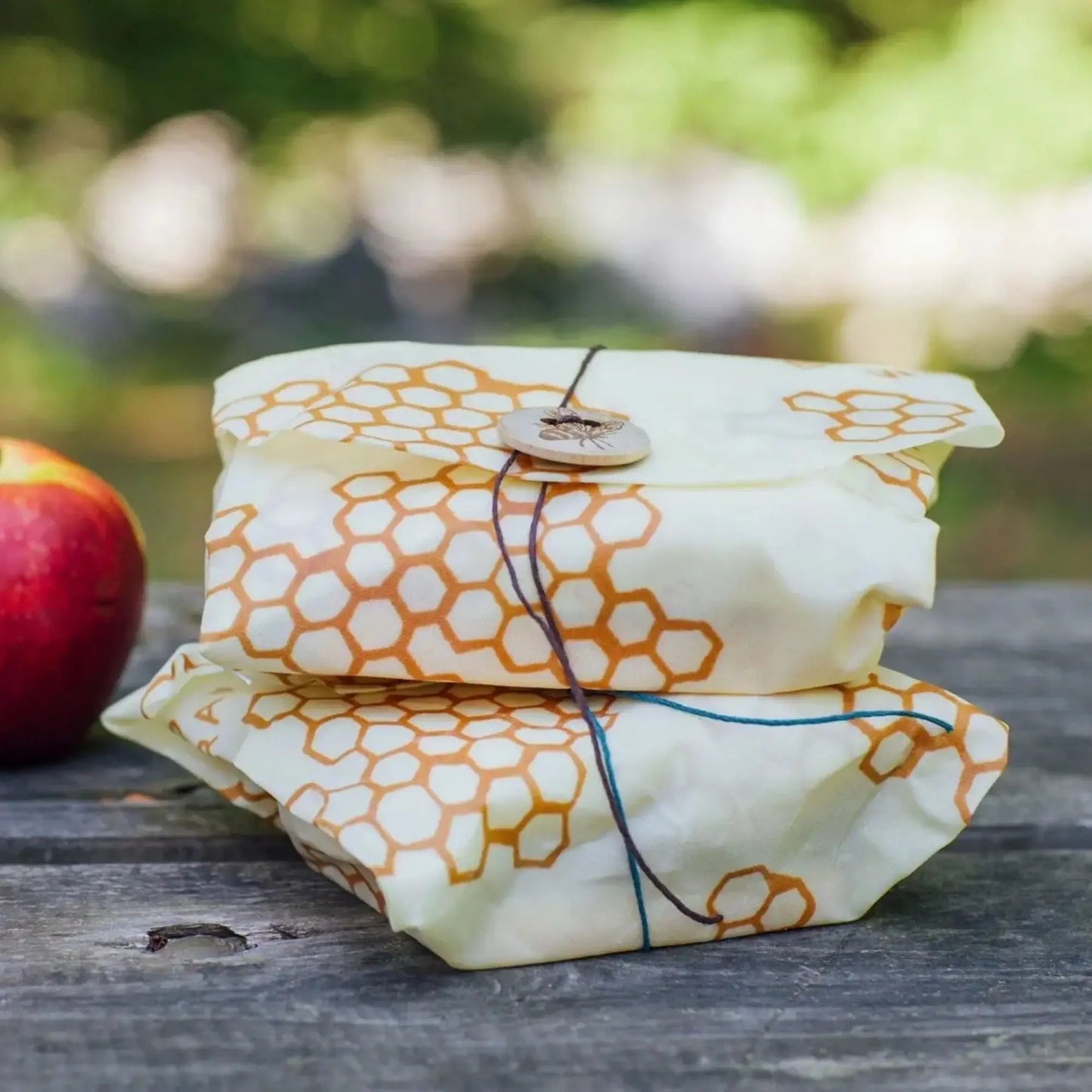 Two wrapped items in beeswax wraps on a wooden surface with a blurred natural background