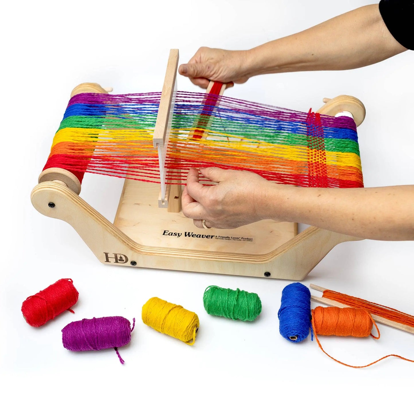 Person weaving rainbow yarn on a wooden rigid heddle table loom