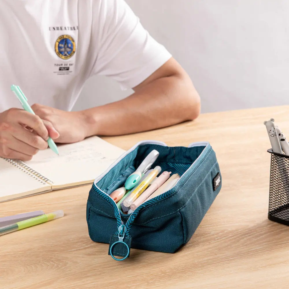Roomy teal pencil case on a desk during writing practice with pencils and school supplies inside