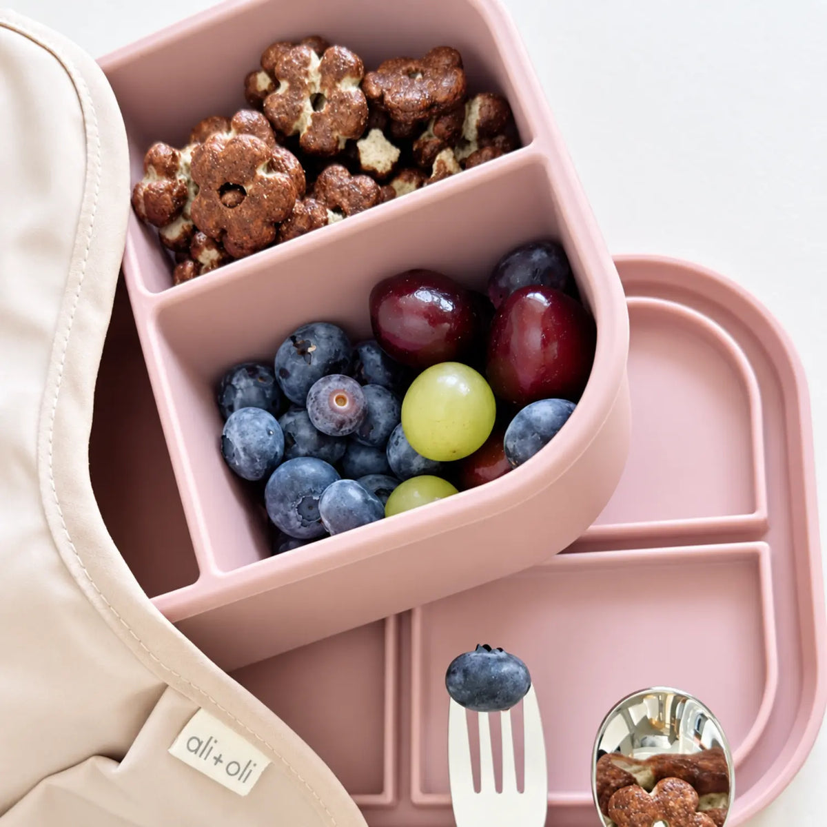 A rose pink bento lunch box shown open with snacks and fruit inside