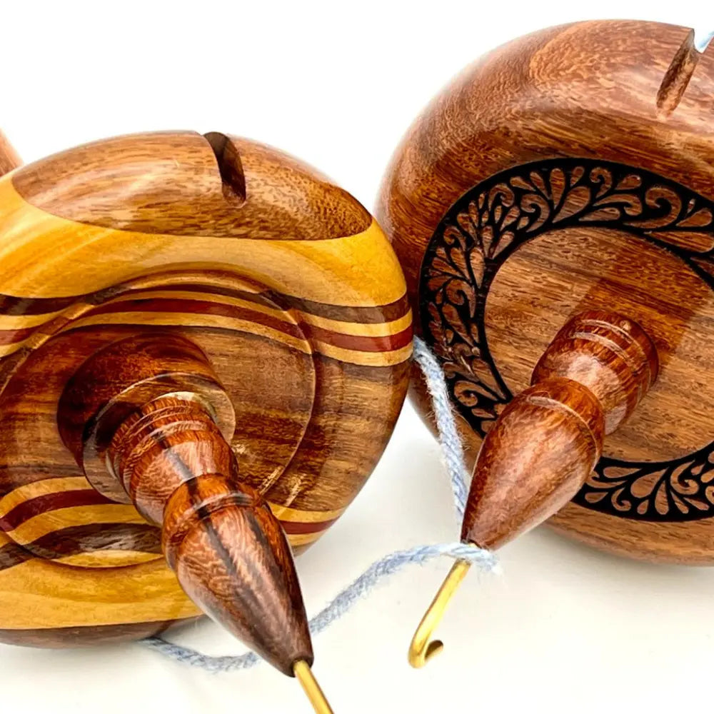 Wooden top whorl drop spindle with white yarn on a white background
